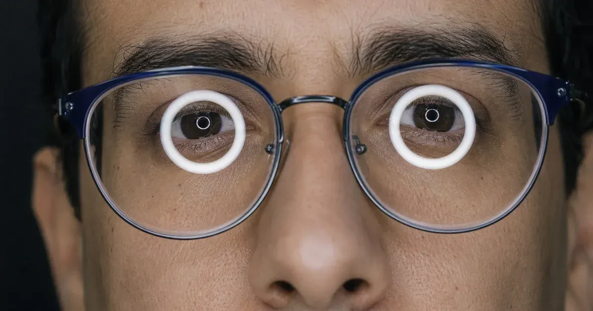 Close-up of eyes behind glasses with a bright circular ring light reflected in both lenses